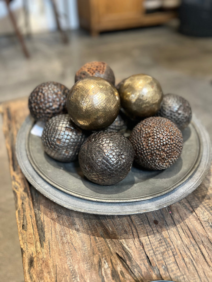 Antique pewter platter holding textured metallic spheres, dark weathered patina