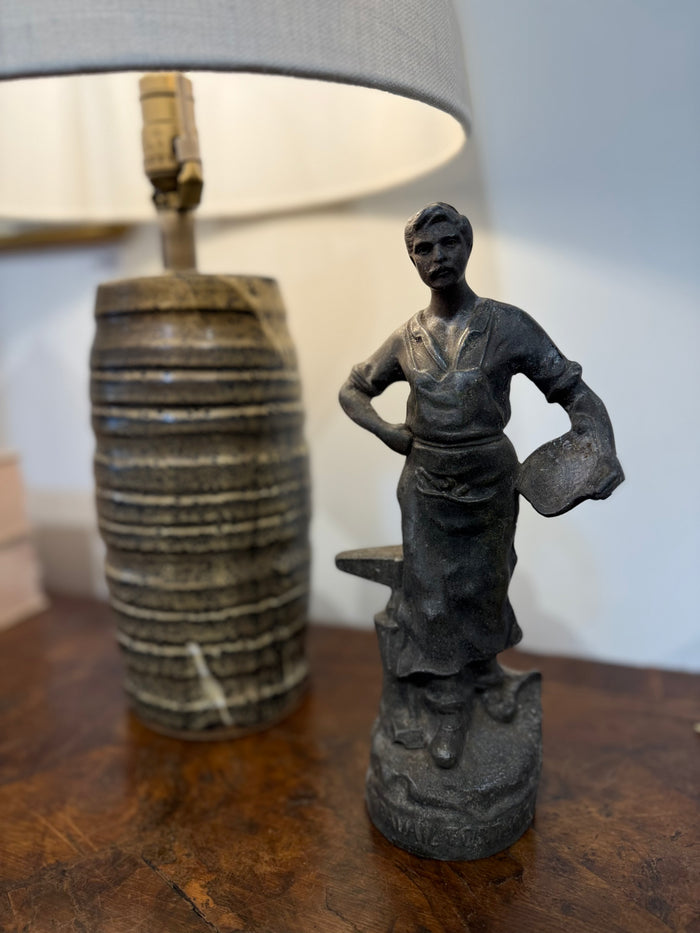 Antique dark cast metal standing woman statue with detailed dress, on a tabletop.
