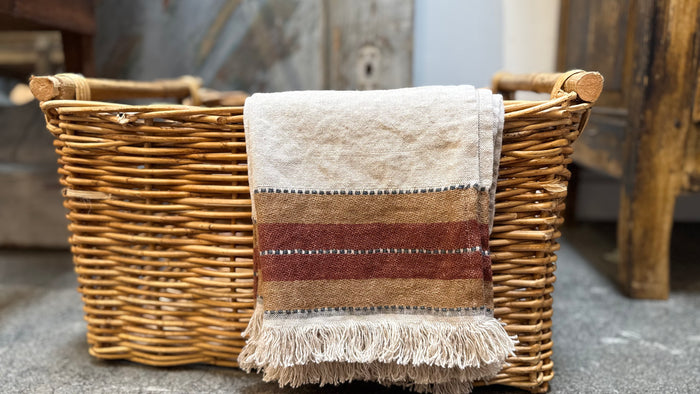 Wicker basket with beige towel, brown stripe, and fringe tassels