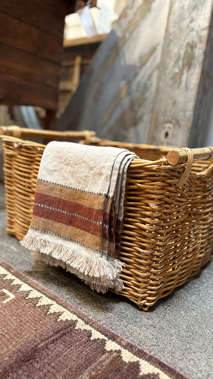 Wicker basket with folded cloth towel, brown stripe, and tassels