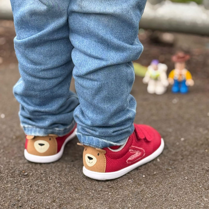 Toddler wearing red mesh trainers with bear on