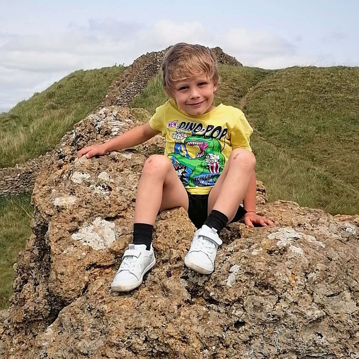 Child sitting on a rock with a scenic background wearing white barefoot trainers