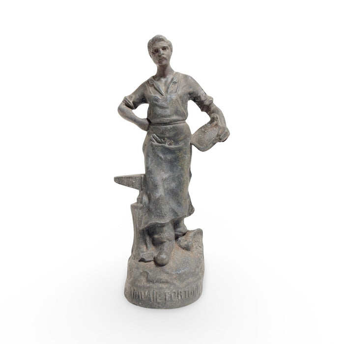 Antique cast metal woman statue holding a short tool, standing with apron-like dress.
