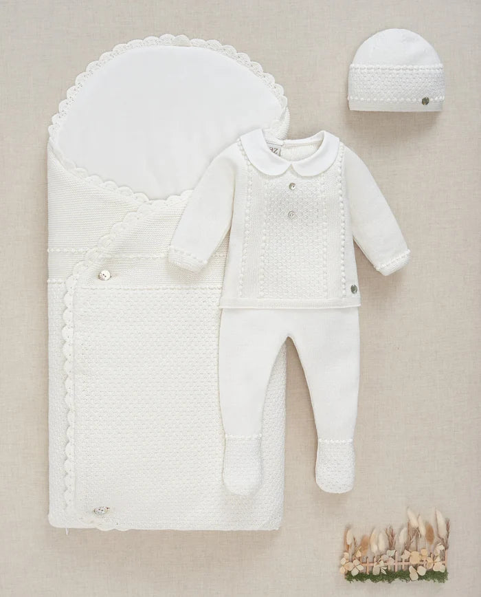 White baby outfit with hat and baby nest on a beige background