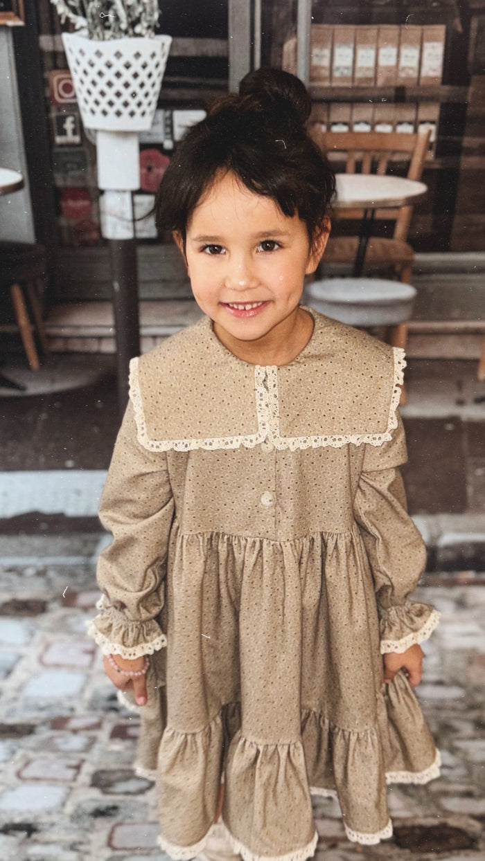 Young girl in a brown dress with lace trim standing on a stone path.