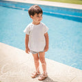 Child standing by a pool with a stone wall and grass in the background