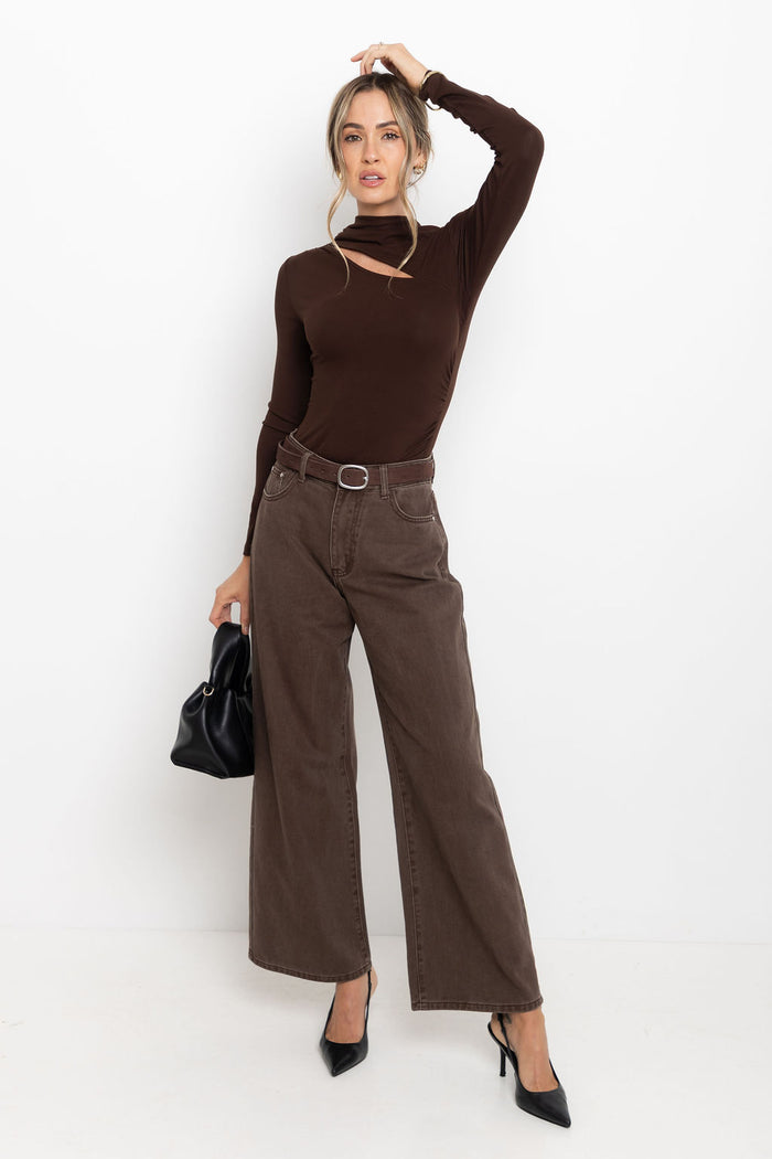 Woman wearing a brown long-sleeve top and wide-leg pants, holding a black handbag on a white background.