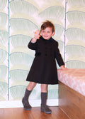 Child wearing a navy coat standing in front of a patterned wall.