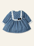 Blue dress with white ruffled collar and black bow on a beige background