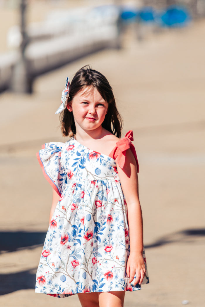 Young girl in a floral dress standing on a sandy beach.