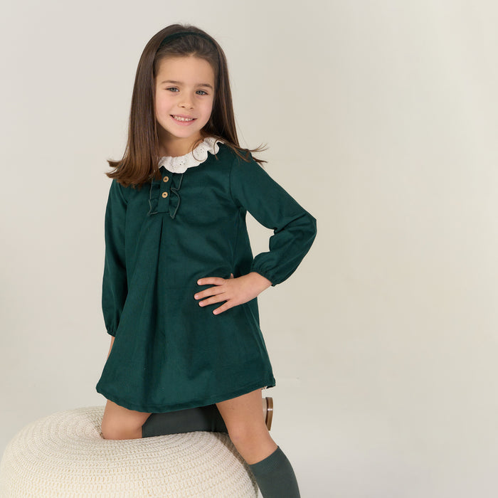 Young girl wearing a green dress with a white collar on a plain background