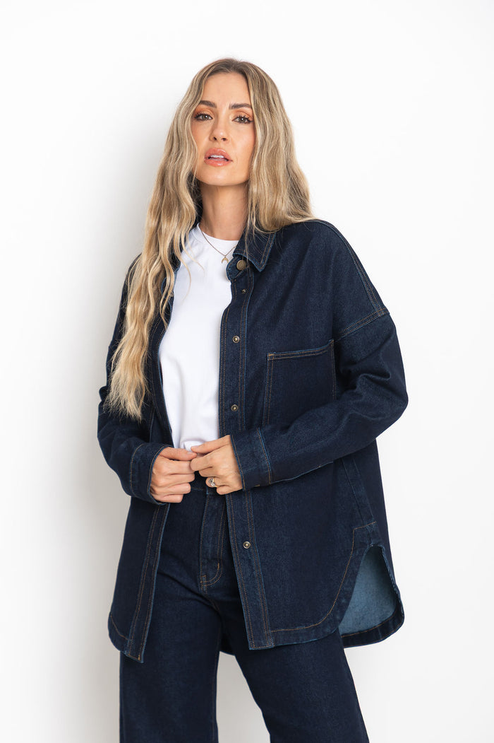 Woman wearing a dark denim jacket over a white shirt on a white background