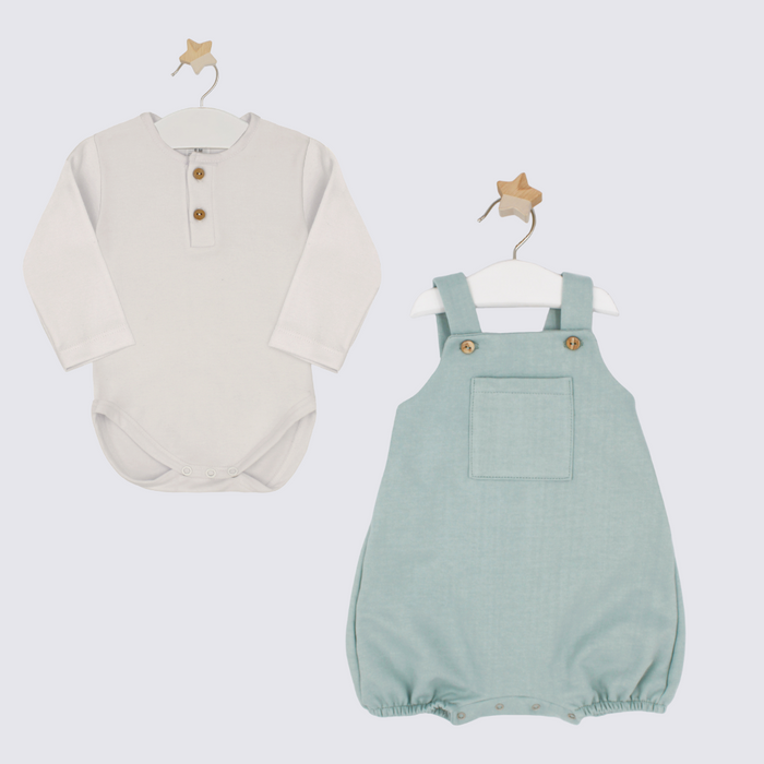 White baby shirt and green overalls on hangers against a white background