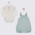 White baby shirt and green overalls on hangers against a white background