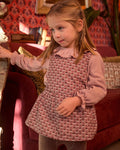 Young girl wearing a pink patterned dress in a room with red and gold decor.