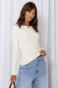 Woman wearing a white long-sleeve top with light-wash wide-leg jeans and a brown belt, carrying a brown handbag, on a white background.