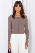 Woman wearing a taupe long-sleeve top with white drawstring pants, on a white background.
