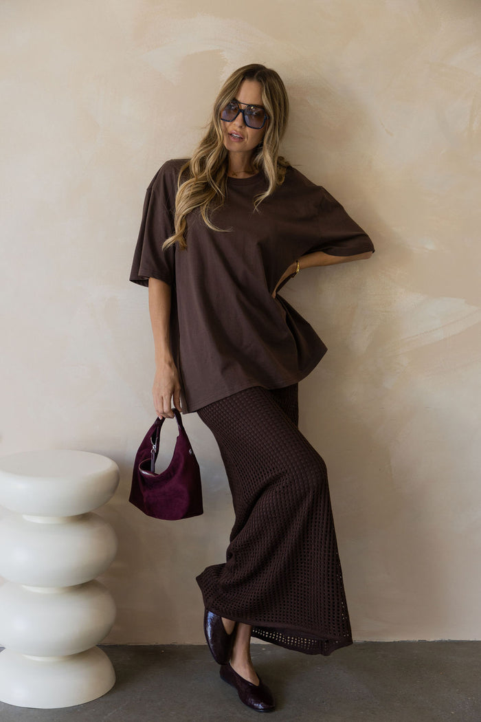 Florence crochet midi skirt in chocolate brown, open-weave knit skirt styled with an oversized brown tee, sunglasses, and burgundy suede bag