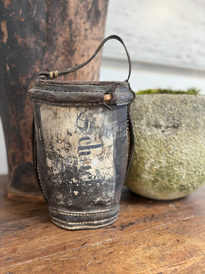 Antique metal water bucket with faded lettering, leather top band, rope carry handle