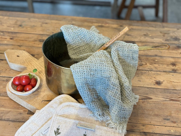 Antique brass pot with long handle, shown with folded light-blue cloth wrap