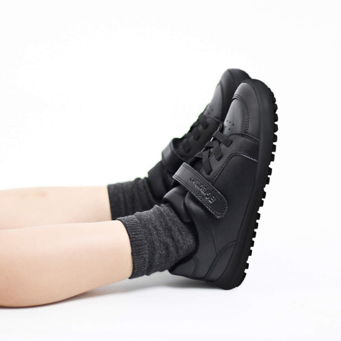 Black sneakers with velcro straps worn by a boy on a white background
