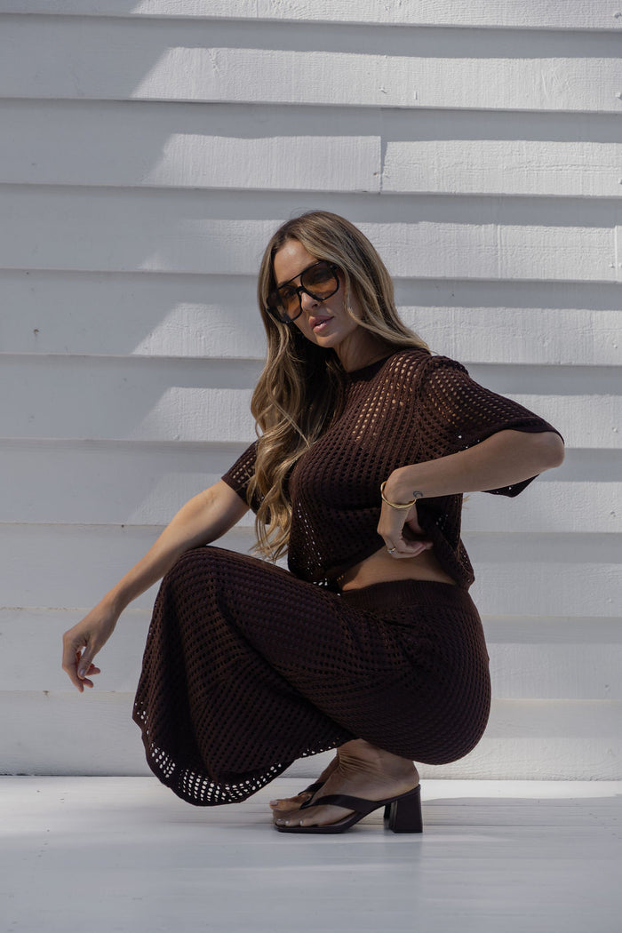 Isabel crochet crop top in brown, cropped open-weave knit top styled with a matching skirt, sunglasses, and heels