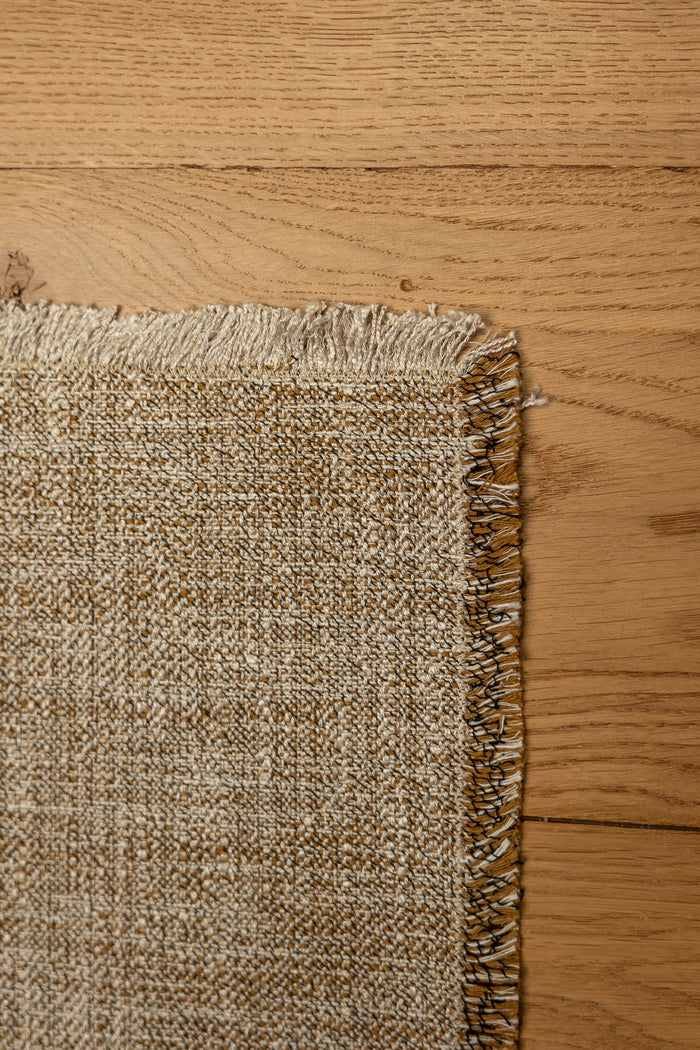 Gray jacquard placemat close-up: textured weave with uneven fringe trim on corner.