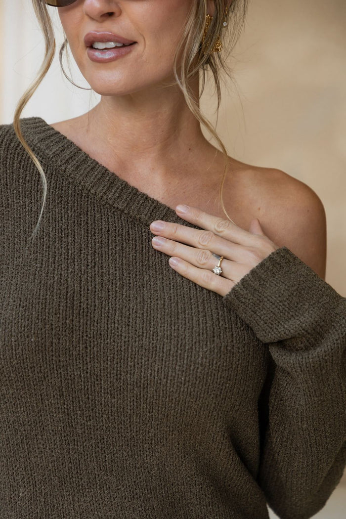 Woman wearing a brown off-shoulder sweater with a neutral background