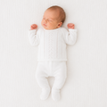 Newborn baby in a white onesie lying on a white textured surface