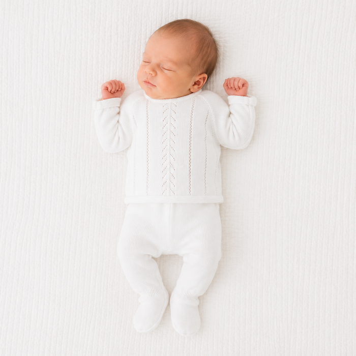 Newborn baby in a white onesie lying on a white textured surface