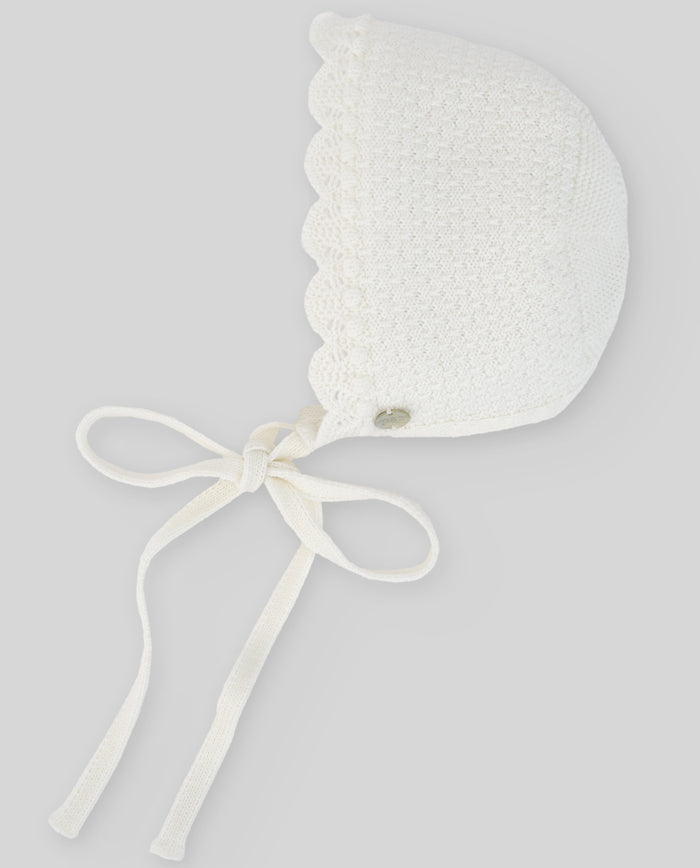 White baby bonnet with a bow on a light gray background