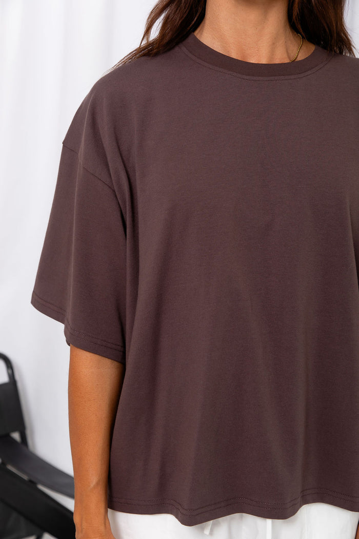 Woman wearing an oversized brown t-shirt with white pants, on a white background.