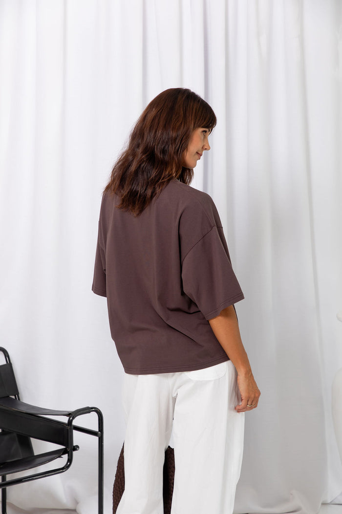 Woman wearing an oversized brown t-shirt with white pants, on a white background.