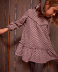 Child wearing a patterned dress against a wooden panel background