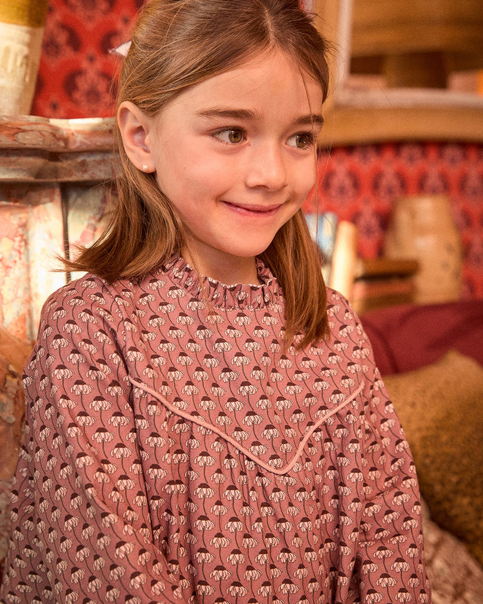 Young girl wearing a pink patterned dress in a warm-toned indoor setting