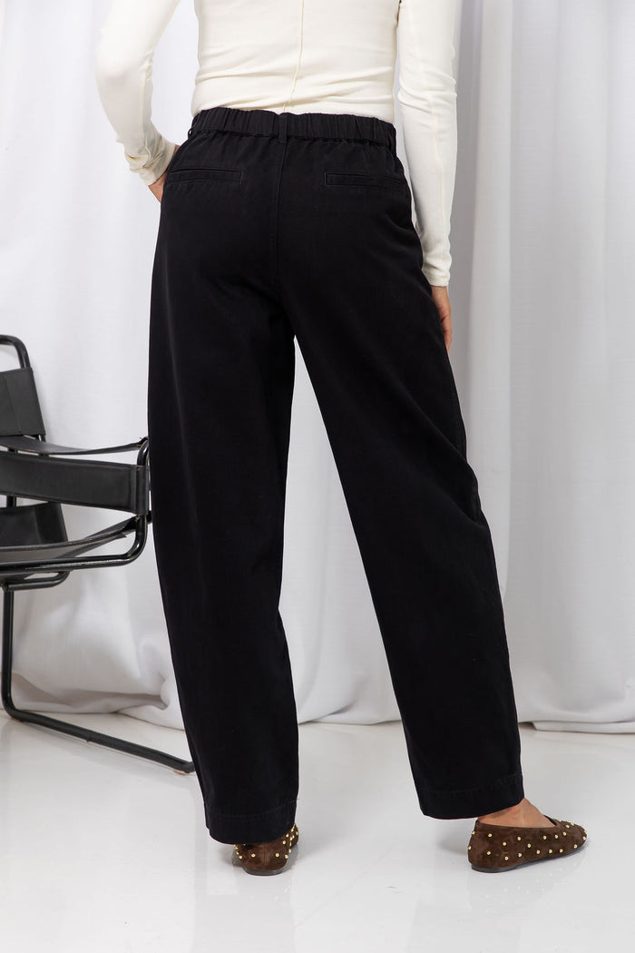 Woman wearing a white long-sleeve top with black tailored trousers, carrying a brown suede bag, on a white background.
