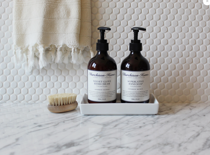 Two hand cream bottles with black pumps on tray, plus cleaning brush