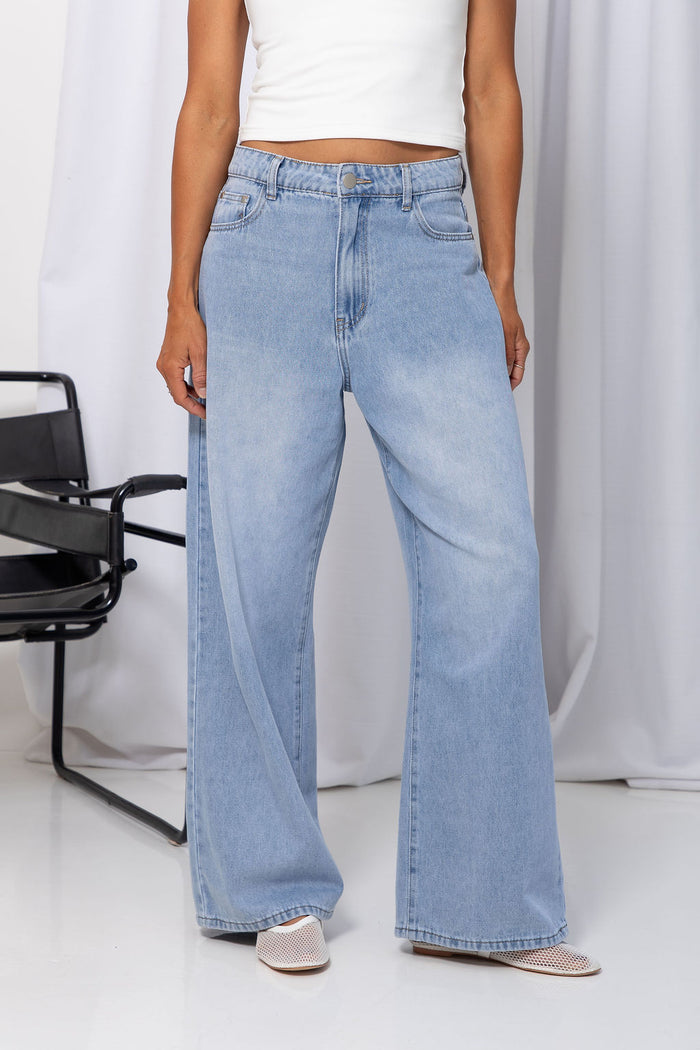 Woman wearing light-wash wide-leg jeans with a white crop top, on a white background.