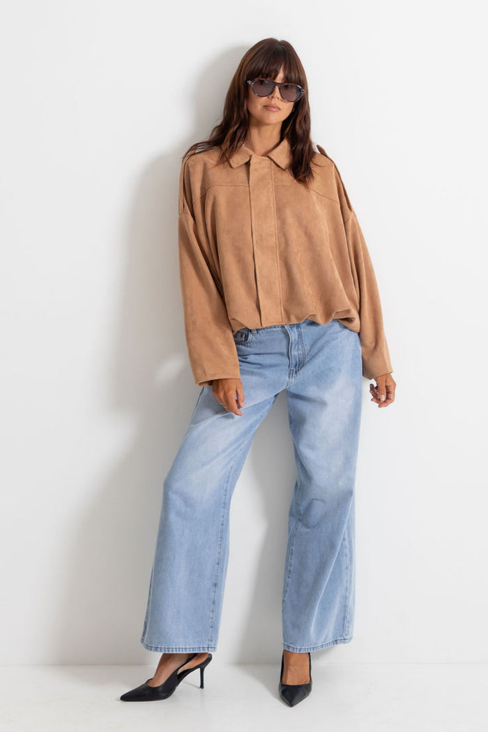 Woman wearing light-wash wide-leg jeans with a sand jacket and black pointed heels, on a white background.