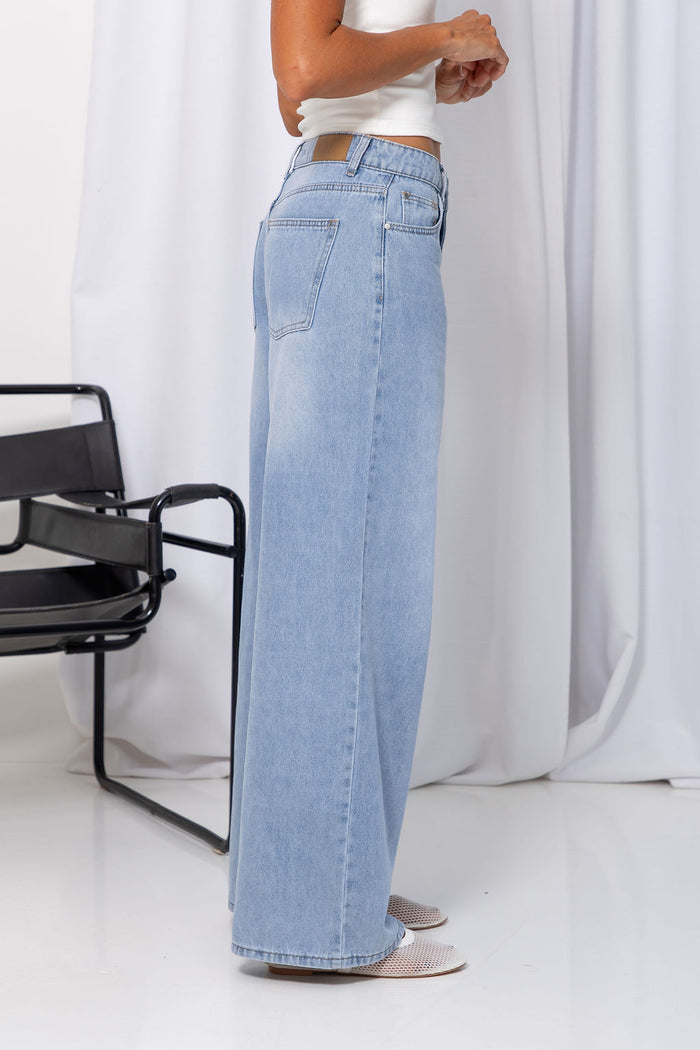 Woman wearing light-wash wide-leg jeans with a white crop top, on a white background.