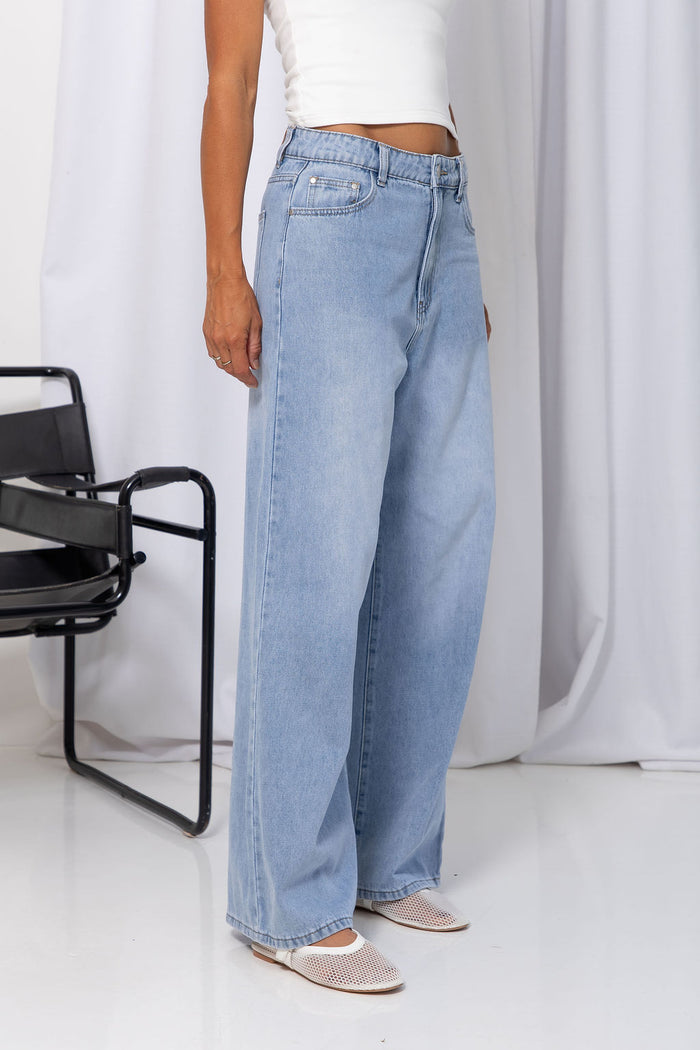 Woman wearing light-wash wide-leg jeans with a white crop top, on a white background.