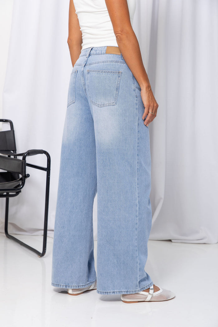 Woman wearing light-wash wide-leg jeans with a white crop top, on a white background.