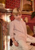 Young boy sitting on a wicker stool in a room with patterned wallpaper and a red couch.