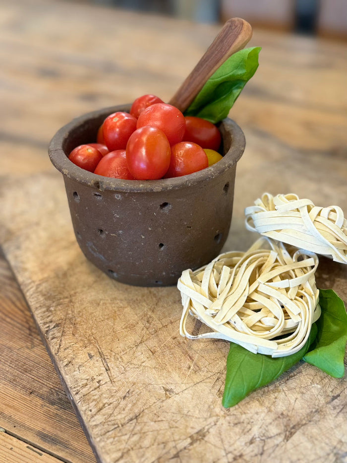 Rust-brown perforated cheese mold cup filled with tomatoes and tied pasta