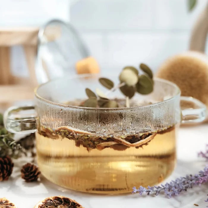 Clear glass stovetop simmer pot filled with herbs in warm amber infusion