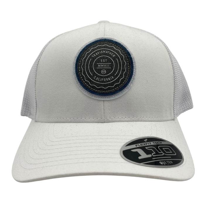 TravisMathew FlexFit Tech "The Patch" hat, style #1M8296, in a close-up showing the hat's fabric and embroidered patch detail.