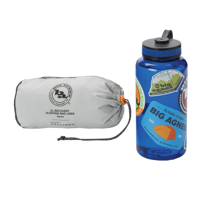 A compact gray Big Agnes Returns UL Recovery Sleeping Bag Liner in a stuff sack sits beside a blue water bottle decorated with colorful stickers.