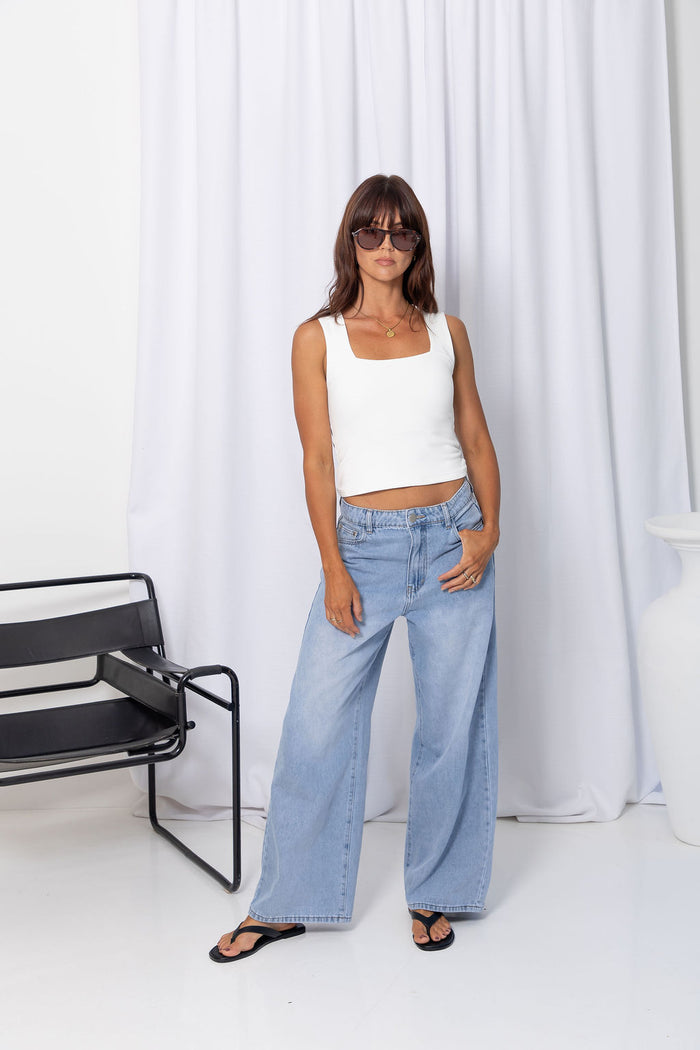 Woman wearing a white square-neck tank top with light-wash denim jeans, on a white background.