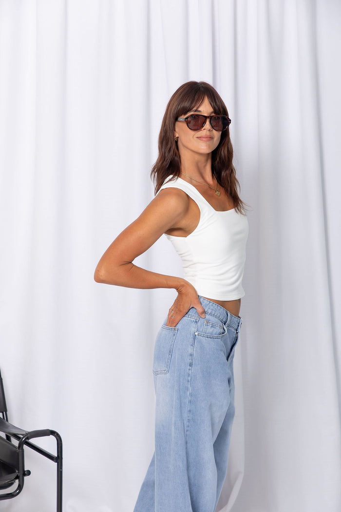 Woman wearing a white square-neck tank top with light-wash denim jeans, on a white background.
