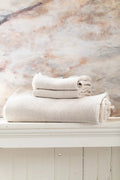 Light ecru waffle hand towel set with fringed edges, neatly stacked on a shelf.